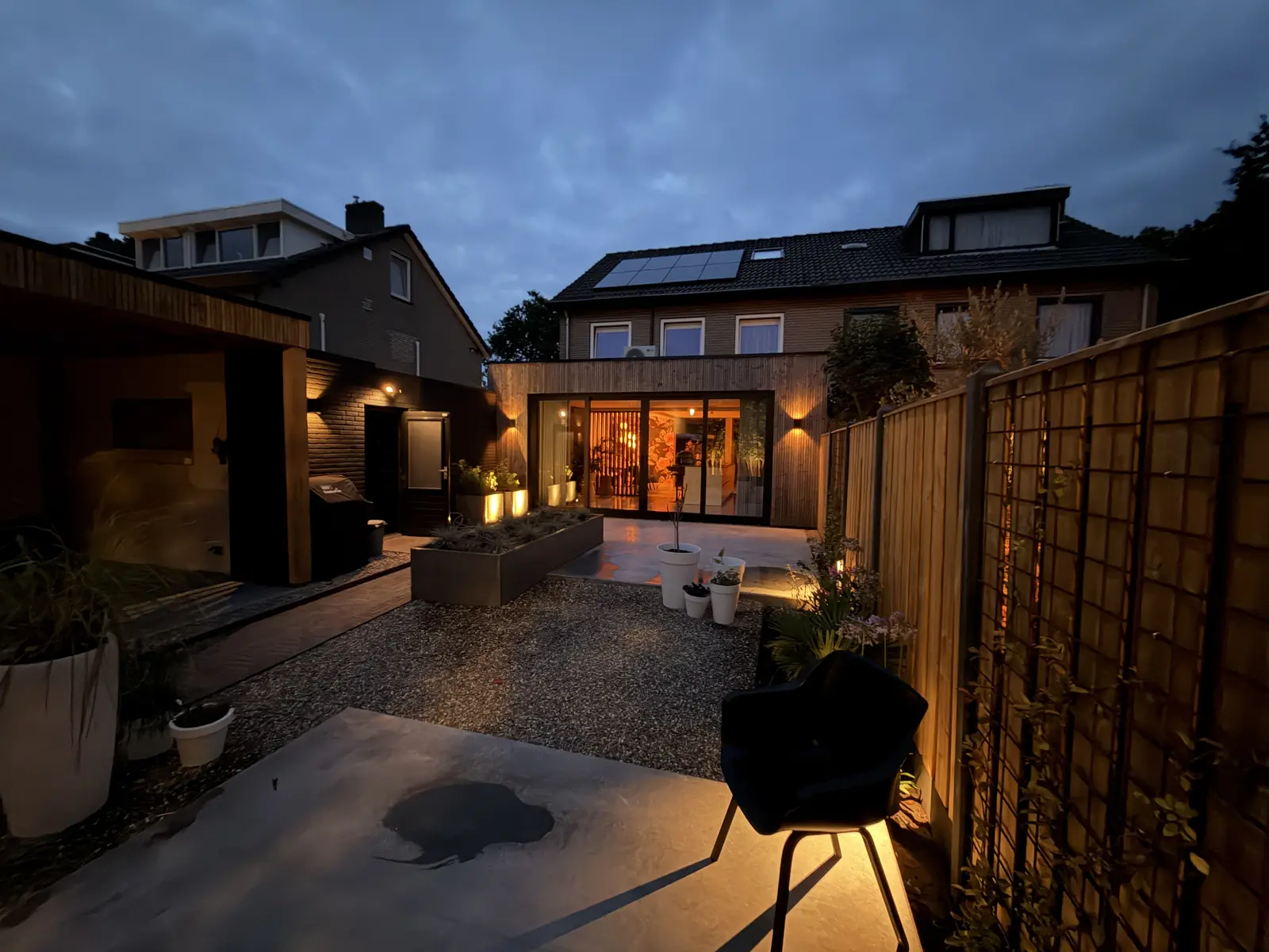 Avondbeeld van de tuin met plantenbakken, beplanting en warme verlichting